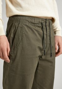 Olivově zelené cargo kalhoty s elastickým pasem, šňůrkou, postranními kapsami a kontrastním šitím. Vyrobené z lehkého, hladkého materiálu.