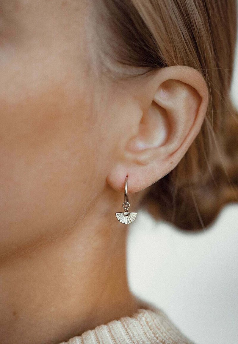 Boucle d'oreille en métal avec un pendentif en forme de éventail, arborant un motif texturé et un petit accent rond en haut. La couleur semble être argent.