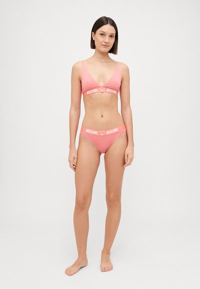 Rozā bralets un bikinī komplekts, kas izgatavots no mīksta auduma. Bralets ir ar dziļu V veida kakla izgriezumu; abiem gabaliem ir kontrastējoša balta lente ar logo.