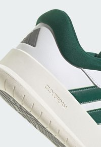 White sneaker with green accents, featuring a textured upper, padded collar, and a cushioned outsole labeled "CLOUDFOAM."