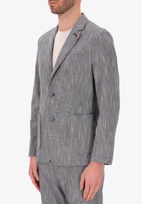 Blazer a righe grigie e bianche, chiusura con due bottoni, rever a soffietto, tessuto strutturato, tasche laterali, indossato sopra una camicia di colore chiaro.