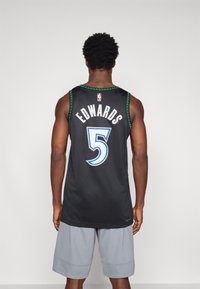Camisola de basquetebol preta com detalhes verdes, apresentando "EDWARDS" e o número "5" em azul. Corte largo, usado com calções cinzentos.