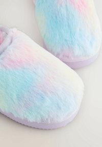 Paire de chaussons duveteux aux couleurs pastel arc-en-ciel avec des semelles lavande sur un fond neutre, montrant les vues de face et de côté.