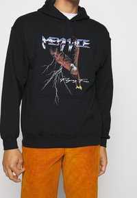 Sudadera negra con un gráfico colorido de un águila, rayos y el texto "Volando Libre". Hecha de material suave y con un bolsillo frontal.