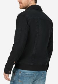 Schwarze Jeansjacke mit klassischem Kragen, geripptem Bündchen und Saum, ausgestattet mit einer aufgesetzten Tasche am Ärmel. Glatte Textur in einfarbig.