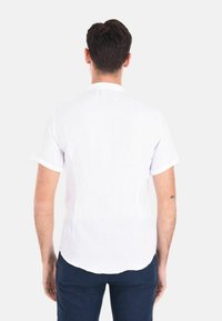 Camicia bianca a maniche corte, realizzata in tessuto leggero. Presenta un colletto classico e un orlo curvo. Texture liscia e design semplice.