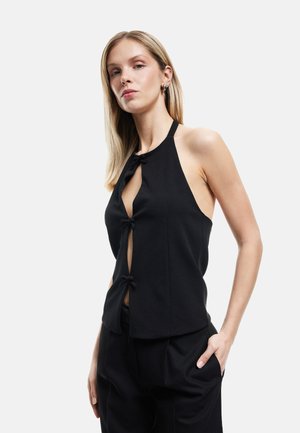 Haut halter noir avec un décolleté en V profond, deux nœuds décoratifs à l'avant, et une coupe ajustée, associé à un pantalon noir taille haute.
