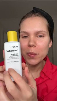 Hvit flaske med gul kork merket "D.Lab Ceramidin Skin Barrier Emulsion." Designet er elegant med matt finish og minimal tekst.