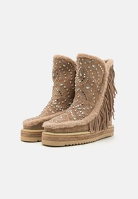 Bottines en suède tan avec des détails en franges, ornées de clous en argent et en turquoise. Doublure épaisse et moelleuse et semelle en wedge texturée.