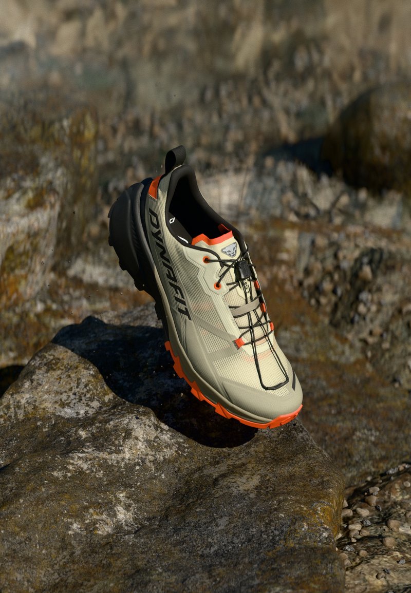 Ελαφρύ γκρι αθλητικό παπούτσι με μαύρες λεπτομέρει ες και πορτοκαλί σόλα. Διαθέτει άνω μέρος από πλέγμα και σύστημα δέσιμο για σταθερότητα.