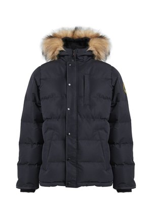 Tienerjongen staat, draagt een zwart gewatteerde winterjas met bontkraag, zwarte broek met een grijze lap en zwarte sportschoenen met groene zolen.
