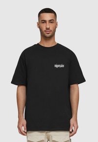 Sort bomulds t-shirt med korte ærmer, med hvid trykt tekst på venstre brystområde. Løs pasform med rund halsudskæring.