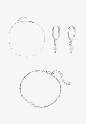 Zarter silberner Kettenarmband mit einer kleinen Perle am Handgelenk, gezeigt von einer Hand mit hellbeigen lackierten Nägeln.