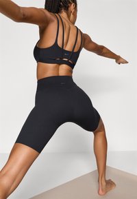 Μαύρο αθλητικό σουτιέν με πολλούς λεπτούς ιμάντες και μαύρο σορτς ψηλόμεσο. Ομαλή υφή, σχεδιασμένο για κίνηση και άνεση.