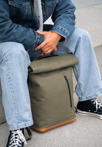 Rolltop-Rucksack in Olivgrün, gefertigt aus glattem, wasserdichtem Material, mit vorderer Reißverschlusstasche, hellem Boden und schwarzen Akzenten.