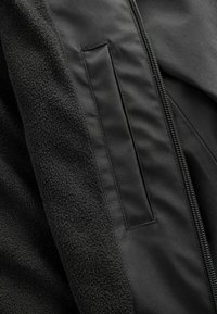 Schwarze Jacke aus einer Mischung aus glattem Stoff und strukturiertem Fleece, mit einem Reißverschluss und einem versteckten Taschenpanel.