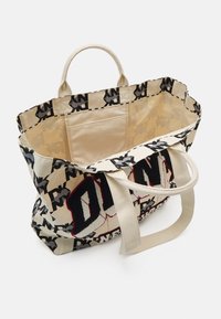 Sac fourre-tout en toile avec logo "DKNY" répétitif noir et blanc, grande étiquette "DKNY" sur le devant, poche intérieure beige et deux anses beiges.