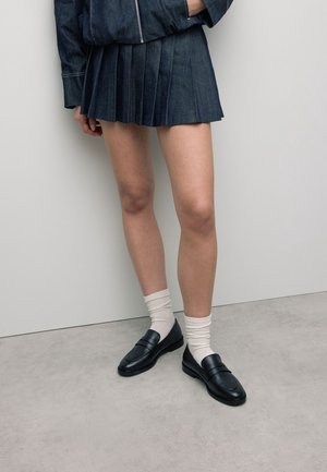 Sorte læder loafers båret med hvide sokker, parret med en denim plisseret nederdel og jakke. Glat tekstur; minimalistisk design med diskret syning.