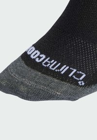 Calcetín deportivo negro y gris con un acabado texturizado, puntera reforzada y nombre de la marca impreso en blanco a lo largo del borde superior.