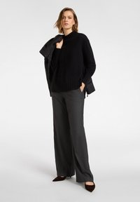 Mustavillinen neulepaita, jossa on korkea kaulus ja ribbireunus, yhdistettynä harmaisiin leveälahkeisiin housuihin ja tummanruskeisiin kärkitossuihin. Malli pitää takkia.