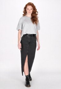 Top grigio a maniche corte abbinato a una gonna di jeans nera con uno spacco frontale, indossato con stivali neri con lacci. Design semplice e casual.