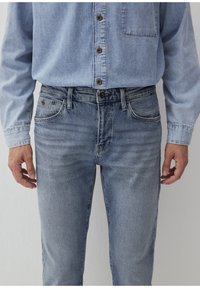 Helle blaue Denim-Jeans mit einer glatten Textur, die ein klassisches Fünf-Taschen-Design, einen Frontknopfverschluss und dezente Ausbleichungen aufweisen.