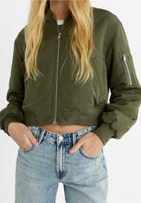 Kort gesneden bomberjack in olijfgroen met een ritssluiting aan de voorkant, geribbelde manchetten en zijzakken, gecombineerd met een hooggetailleerde, distressed blauwe jeans.