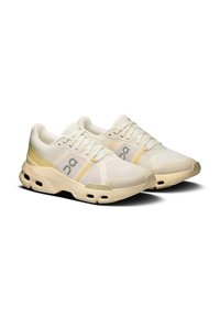 Jasno beżowe buty sportowe z przewiewną siateczką, gumową podeszwą i wyściełanym kołnierzem. Posiadają logo oraz subtelne akcenty w kolorze żółtym.