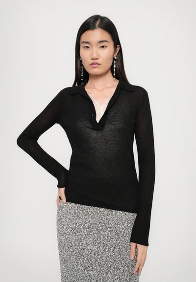 Un top negru cu mâneci lungi, dintr-un material ușor și transparent, cu guler, deschidere cu nasturi și un design ajustat, asortat cu o fustă gri cu model.
