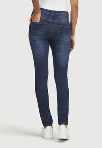 Schlanke dunkelblaue Jeans mit Gesäßtaschen, aus Denim gefertigt. Verfügt über ein enges Design und wird mit weißen Sneakern kombiniert.