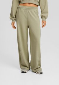 Gröna sweatpants med en avslappnad passform, elastisk midja och muddade anklar, tillverkade av mjukt material, i kombination med grå sneakers.