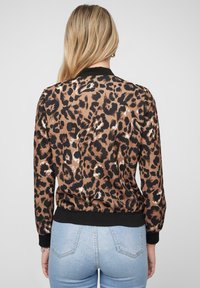 Giacca bomber con stampa leopardata in marrone e nero, presenta un colletto e polsini ribattuti neri, realizzata in un tessuto leggero e liscio con orlo elasticizzato.
