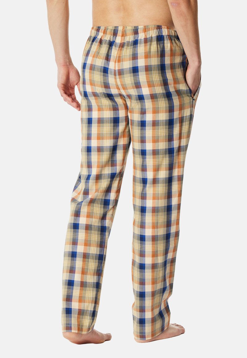 Personne debout pieds nus portant un pantalon de pyjama à carreaux beige, orange et bleu avec une taille élastique et les mains dans les poches, vue de dos.