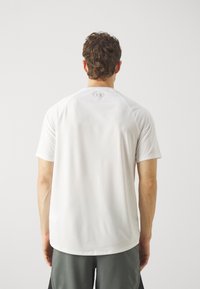 Camiseta deportiva blanca de manga corta con mangas raglán, textura suave, logo sutil en la parte trasera, combinada con pantalones cortos grises.