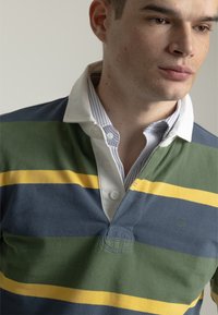 Camisa polo con cuello que presenta rayas horizontales en azul marino, verde y amarillo. Fabricada en una tela suave con un detalle de logo texturizado.