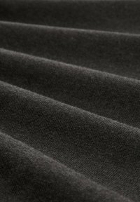 Ciemnoszara tkanina o miękkiej, teksturowanej powierzchni, złożona w delikatne fale, ukazująca subtelne różnice w odcieniach i drobne wzory dzianiny.