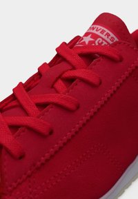 Κόκκινο σουέντ αθλητικό παπούτσι με κόκκινα κορδόνια και ορατό λογότυπο Converse στη γλώσσα, με λεπτομερή ραφή και λευκή άκρη σόλας.