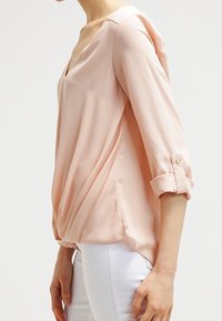 Vaaleanpunainen, kevyt paita V-puolikauluksella ja käännetyllä hihalla. Ominaisuuksiin kuuluu pehmeä laskostus ja sivuaukot rentoa istuvuutta varten.