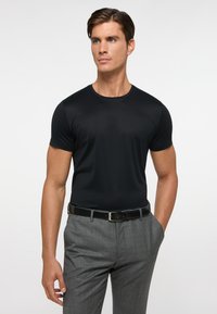 Sort kortærmet t-shirt med rund hals, lavet af et glat stof, parret med grå mønstrede bukser og et sort bælte.
