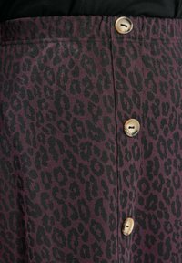 Violetti hame, jossa on leopardikuosiset kuvioinnit, joissa on selkeitä mustia läiskiä ja pyöreitä beigejä nappeja edessä. Pehmeä kangas.