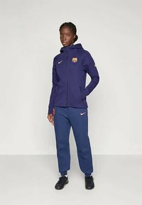 Purple Nike zip-up hoodie with Barcelona logo, paired with dark blue pants, featuring a pink Nike swoosh, and textured fabric throughout.