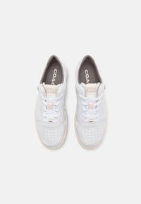 Vita sneakers med en slät läderoversida, perforerat tånät, vita snören, ljusbrun sula och grå innersulor med varumärkeslogotyp.