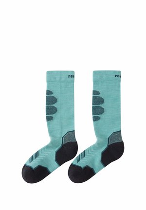 Paar türkisfarbene knielange Socken mit dunkel verstärkter Ferse, Zehe und dekorativen seitlichen Mustern, flach auf weißem Hintergrund gelegt.
