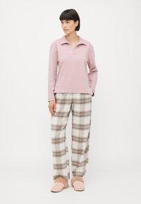 Rosa långärmad topp med polokrage, i kombination med beige rutiga byxor. Mjuka tofflor har en fluffig foder.