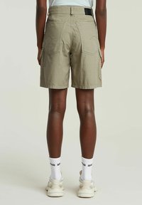 Shorts cargo kaki avec poches latérales doubles, détails cousus et coupe décontractée. Portés avec des chaussettes blanches et des baskets claires.