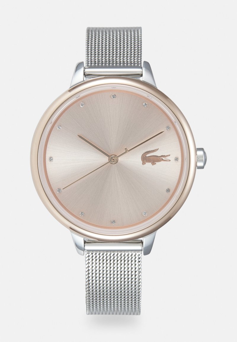 Reloj redondo con bisel en tono oro rosado, correa de malla plateada, esfera metálica taupe y marcadores de hora claros. Logotipo de Lacoste mostrado de forma sutil.