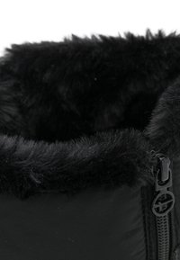 Lähikuva mustasta talvisaappaasta, jossa on pörröinen turkisvuori ja musta vetskari pyöreällä veto-otteella sivussa.