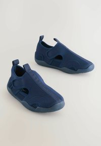 Tmavomodré slip-on topánky s sieťovanými panelmi, flexibilnou gumovou podrážkou a prešitými akcentmi. Obsahujú zadný ťahací jazýček pre jednoduché obutie.