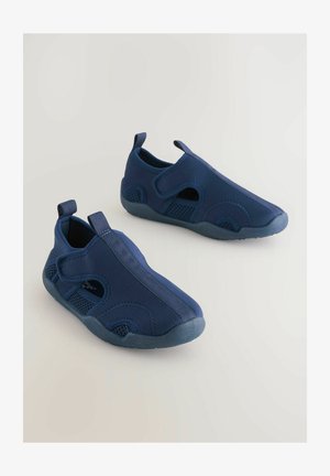 Temno modri natikači z mrežastimi paneli, fleksibilnimi gumijastimi podplati in šivanimi detajli. Imajo zadnji traku za enostavno obuvanje.