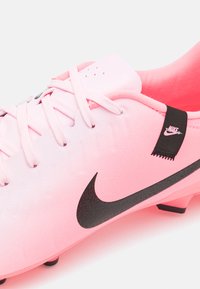 Pink Nike soccer cleat with a smooth upper, black logo, and lace-up design. Features a textured black accent near the heel and molded studs.